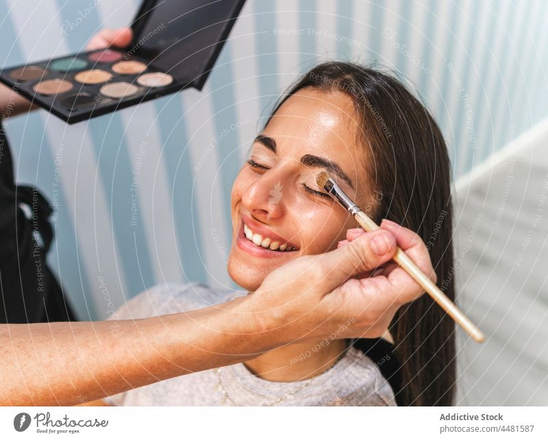 Crop Master trägt Make-up auf das Augenlid einer Kundin auf Frau visagiste Palette Schönheit Model bewerben Bürste Gesicht Lidschatten Kosmetik Lächeln
