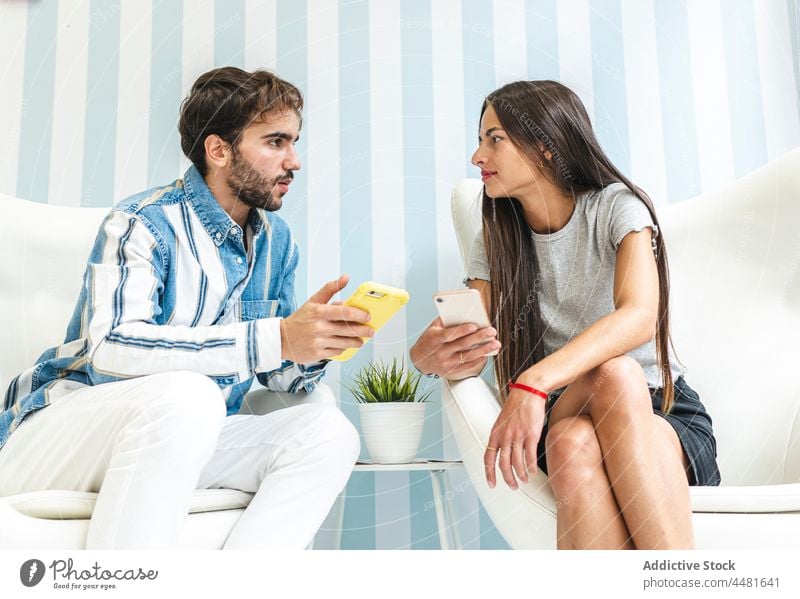 Mann und Frau mit Smartphones sitzen auf Sesseln Funktelefon Armsessel Zusammensein Inhalt Kommunizieren reden benutzend elegant Apparatur Stil Browsen männlich