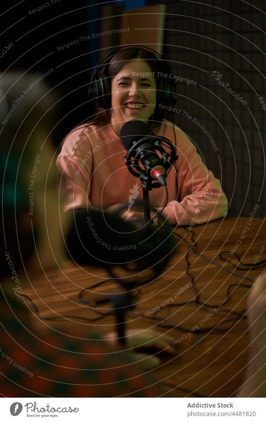 Junge Frau spricht in ein Mikrofon, während sie einen Podcast mit einem Mitarbeiter aufnimmt Aufzeichnen Radio Kommunizieren Lächeln Wirt Arbeit sprechen