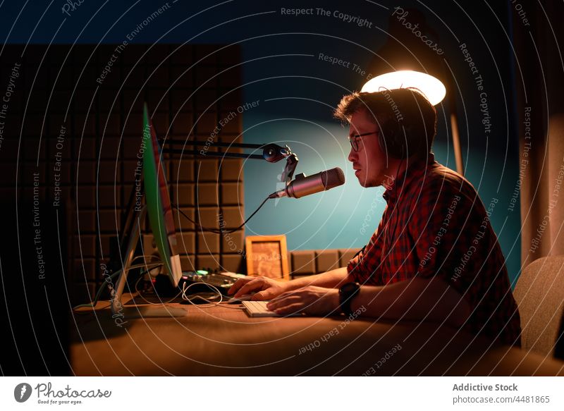 Konzentrierter junger Mann, der an einem Tisch mit Computer und Mikrofon sitzt und einen Podcast erstellt Aufzeichnen Arbeit sprechen Fokus Wirt online Radio