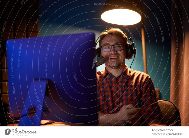 Glücklicher junger Mann, der einen Podcast erstellt, am Tisch sitzend mit Computer und Mikrofon Aufzeichnen Arbeit sprechen Fokus Wirt online Radio strömen