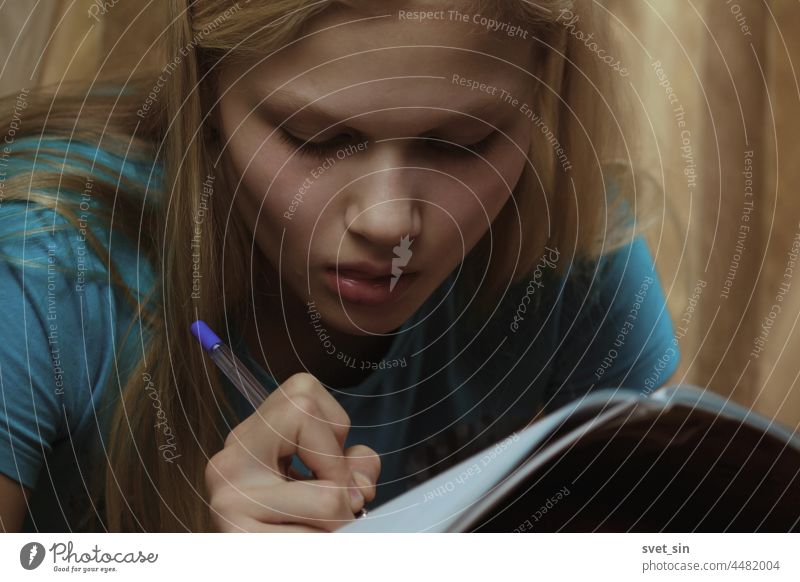 Ein blondes Teenager-Mädchen ist im Haus mit dem Schreiben in einem Notizbuch beschäftigt. im Innenbereich schreiben Schreibstift konzentriert studierend