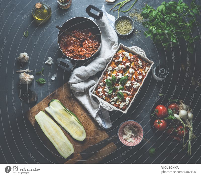 Hausgemachte Zucchinilasagne mit frischem Basilikum, Bolognese, Tomaten, Knoblauch, Olivenöl und Käse in einer weißen Auflaufform auf einem dunklen Küchentisch aus Beton. Kochen italienisches Essen zu Hause. Ansicht von oben.