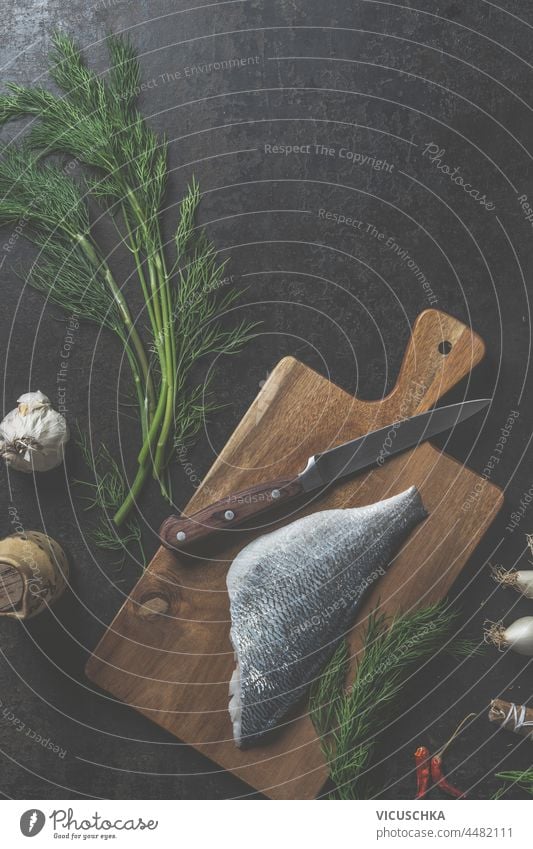 Dorado Fischfilet auf Schneidebrett mit Messer, Dill, Nordseekrabbe und andere Zutaten auf dunklem Küchentisch Hintergrund. Ansicht von oben Filet dunkel Tisch