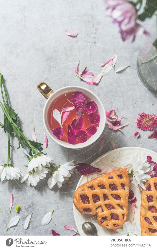 Herzförmiges Gebäck mit Beeren und rosa Blumen Tee in weißer Teetasse auf weißem Beton Küchentisch mit Blumen. Gemütliche, romantische Teezeit zu Hause. Ansicht von oben.