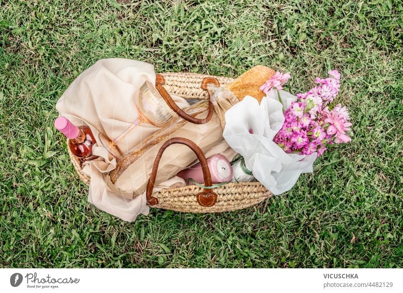 Picknick-Korb mit Wein, Baguette, Weinglas, Blumen, Kerze und Picknick-Decke auf grünem Gras Hintergrund. Romantisches Picknick Vorbereitung im Sommer. Ansicht von oben.