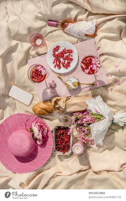 Sommer-Picknick mit frischen Beeren, Baguette, Rosé-Wein und Gläser, Käse und Blumen, rosa Sonnenhut und Kerzen auf beige Tuch. Romantisches Brunch-Konzept mit rosa Themen. Ansicht von oben.