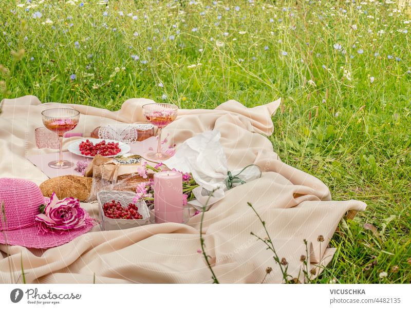 Picknickdecke mit Weingläsern, Rosenwein, Kerzen, Sonnenhut, frischen Beeren und Baguette auf grünem Gras. Romantischer Brunch im Freien mit Essen und Getränken im Sommer. Ansicht von vorne.