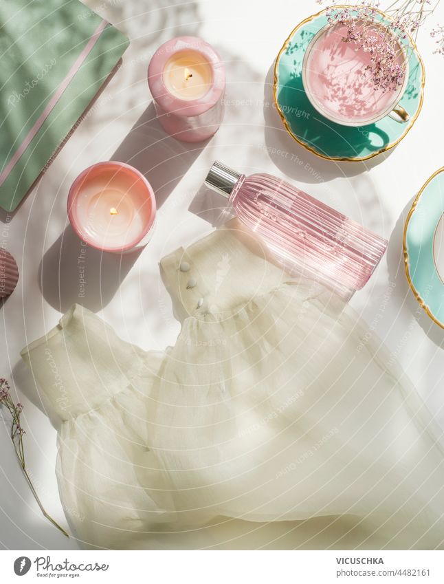 Frauen Morgenroutine mit Tee, Kerzen, Gesichtswasser in Glasflasche, Kleidung, Blumen und Notizblock auf weißem Hintergrund. Gemütlicher Morgen zu Hause mit Schönheitsprodukten. Ansicht von oben.