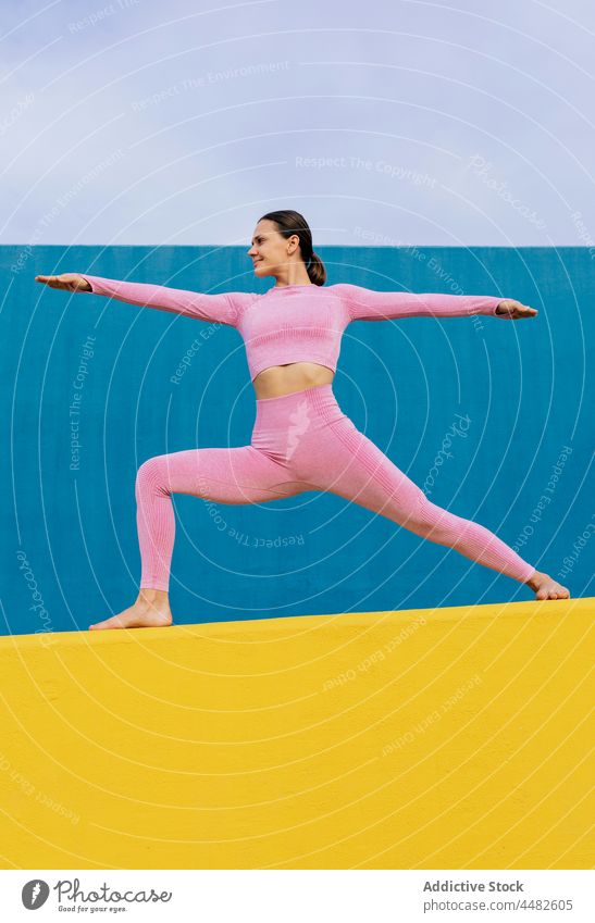 Lächelnde Frau übt Yoga in Kriegerpose beweglich Krieger-Pose Dehnung üben Gleichgewicht heiter Asana virabhadrasana Harmonie Wellness lebhaft Glück Energie