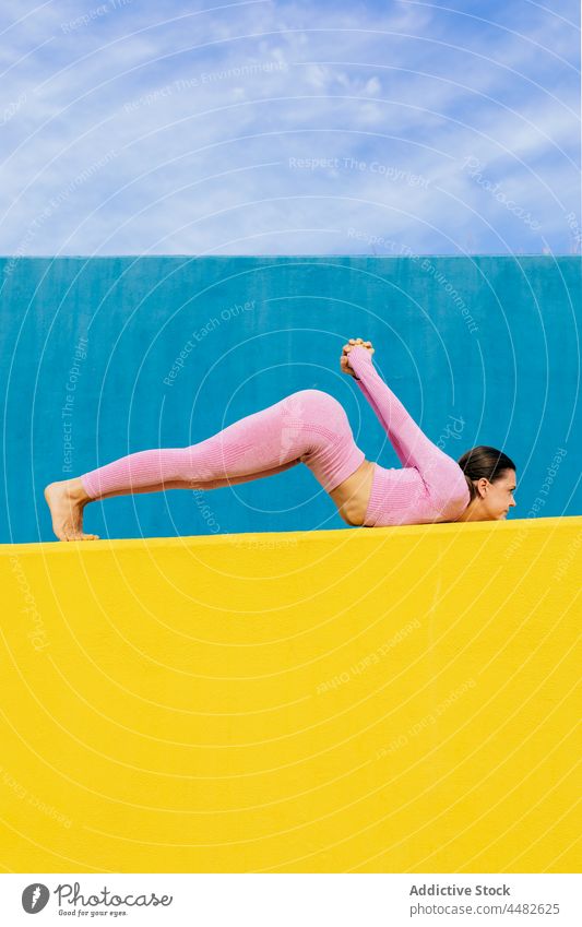 Schlanke Frau macht Yoga-Asana auf blauem und gelbem Hintergrund Dehnung beweglich üben Gleichgewicht Wellness Bein angehoben Körperhaltung Wohlbefinden Pose