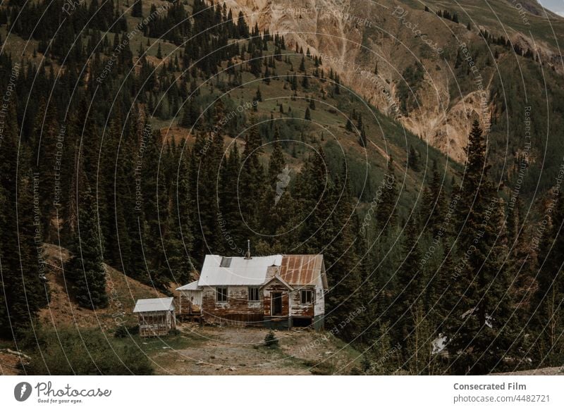 Verlassenes Haus in den Bergen verlassenes Haus Geisterstadt kaputt und ruiniert Holzhaus altehrwürdig reisen Abenteuer Bäume dunkel Stimmung Bergkette