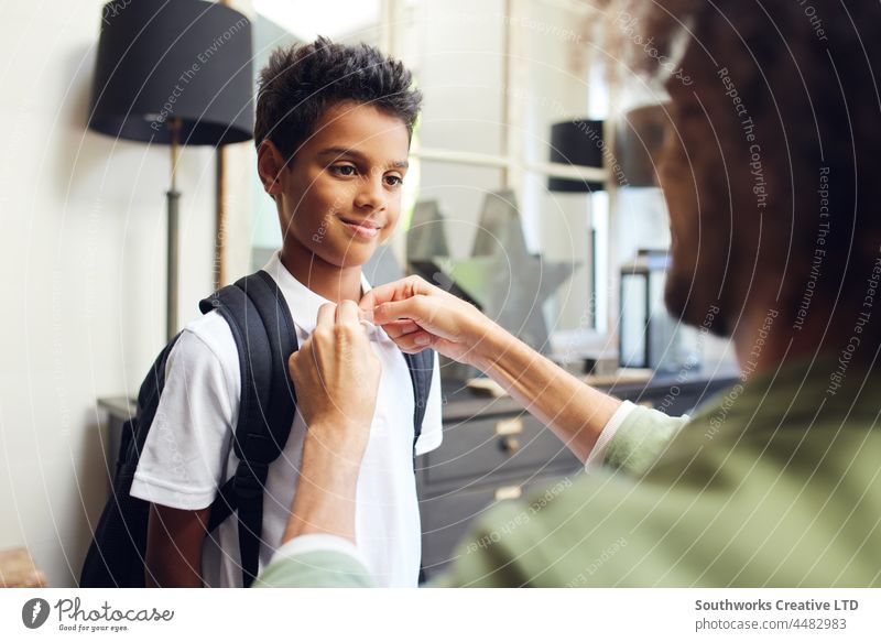 Junge lächelt, als sein Vater sein Hemd zuknöpft Schule gemischte Rasse Lächeln Schaltfläche Hilfsbereitschaft Sohn vorbereiten Unterstützung im Innenbereich
