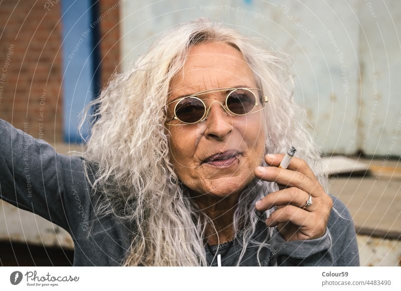 Frau bläst den Rauch einer Zigarette aus Lächeln alte Frau modisch freundlich stylisch mit dem Rauchen aufhören rauchende Frau älter Lifestyle Senior Kaukasier
