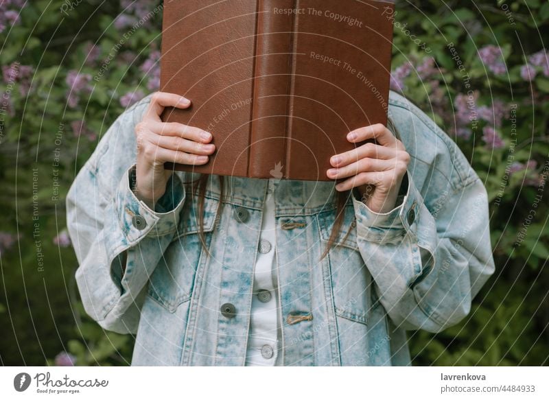 Gesichtslose Aufnahme einer Frau, die sich im Freien ein Buch vor das Gesicht hält Lifestyle jung lesen Porträt Bildung intelligent Stehen grün Sommer Hände