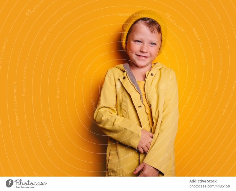 Lachender Junge, der vor gelbem Hintergrund wegschaut Glück heiter Herbst Porträt Jacke Oberbekleidung Beanie froh Freude Stil Kind trendy hell Outfit