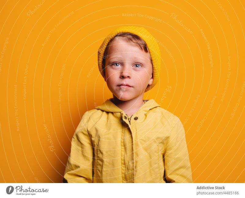 Ruhiger Junge in trendigem Outfit vor gelbem Hintergrund Windstille Kindheit Stil Individualität anhaben Regenmantel Komfortzone Vergnügen wenig trendy Farbe