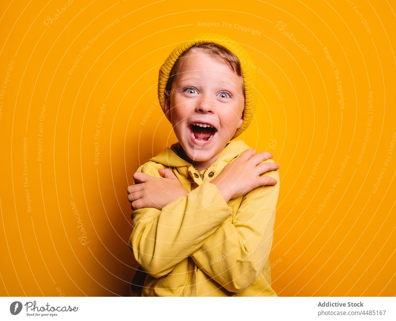 Glücklich lächelnder Junge in trendigem Outfit steht mit verschränkten Armen vor gelbem Hintergrund Umarmung Windstille Umarmen Kindheit Stil Individualität