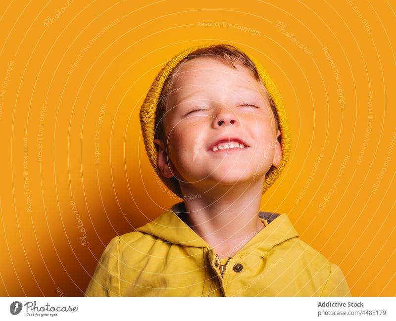 Lachender Junge mit geschlossenen Augen vor gelbem Hintergrund Glück heiter Herbst Porträt Jacke Oberbekleidung Beanie froh Freude Stil Kind trendy hell Outfit