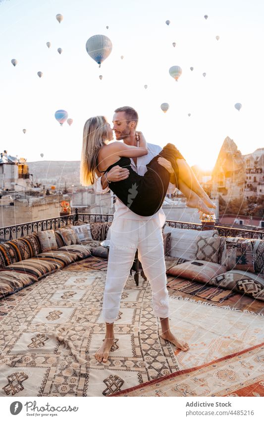 Mann hält Seelenverwandte auf Terrasse gegen Heißluftballons Paar Seelenverwandter Umarmen Ballone Dachterrasse romantisch Zusammensein Liebe Zuneigung