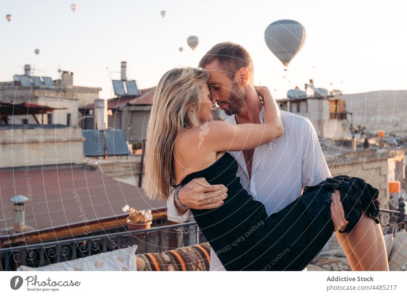 Mann hält Seelenverwandte auf Terrasse gegen Heißluftballons Paar Seelenverwandter Umarmen Ballone Dachterrasse romantisch Zusammensein Liebe Zuneigung