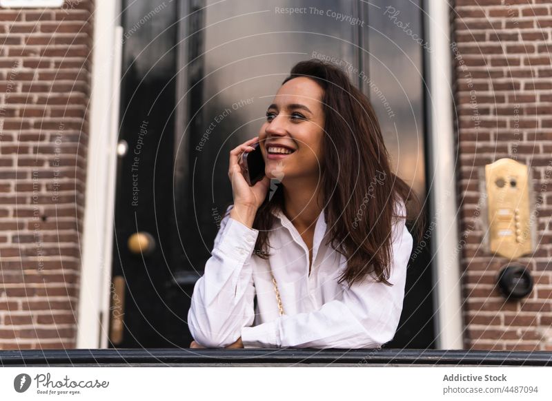 Lächelnde Frau beim Telefonieren auf der Straße Gebäude Smartphone Eingang Glück Gerät benutzend Apparatur Browsen online Mobile urban jung Geländer positiv