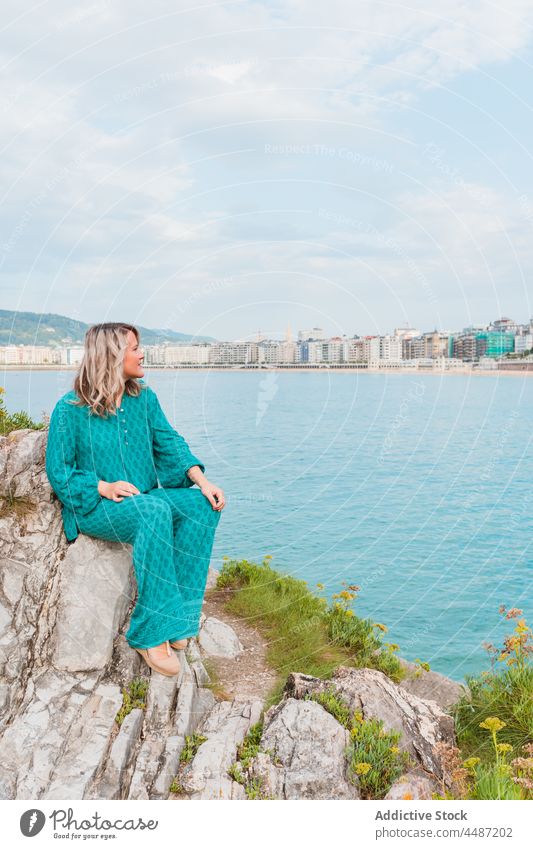 Verträumte Frau sitzt auf Felsen mit grünen Pflanzen in der Nähe des Meeres Stil Natur positiv verträumt ausrichten MEER Umwelt donostia trendy San Sebastián