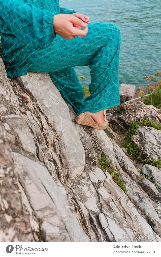 Anonyme fröhliche Frau sitzt auf einem Stein vor dem Meer und den grünen Hügeln heiter Stil Borte Felsen Harmonie Spanien San Sebastián Baskenland Biskaya-Bucht