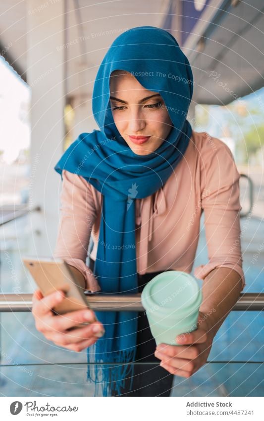 Muslimische Frau mit Kaffee zum Mitnehmen und Smartphone Imbissbude Großstadt Browsen Hijab Mobile Telefon ethnisch arabisch muslimisch Straße online Nachricht