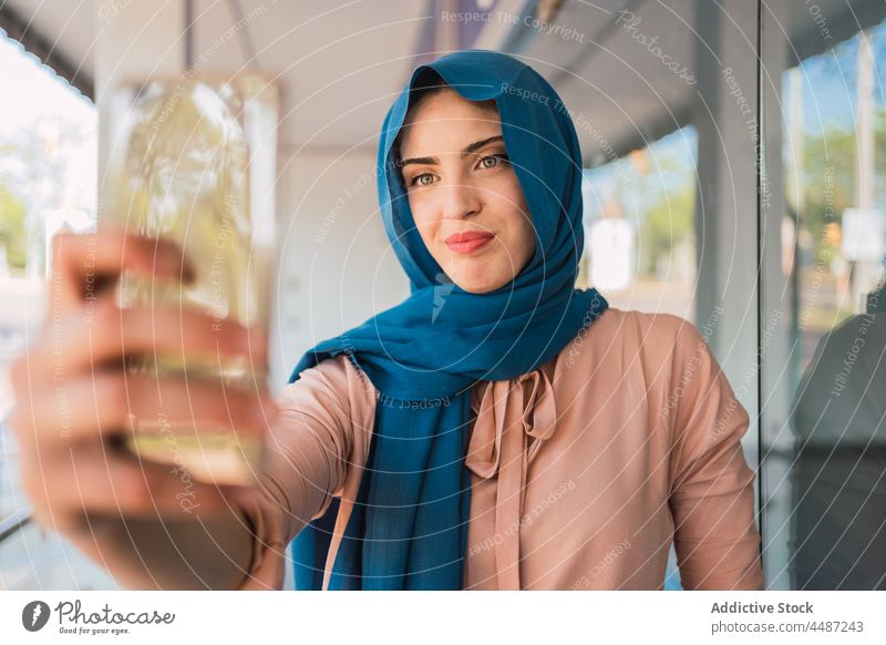 Lächelnde muslimische Frau macht Selfie in der Stadt Smartphone Hijab Imbissbude Selbstportrait Tradition Großstadt arabisch ethnisch Straße Kopftuch Glück
