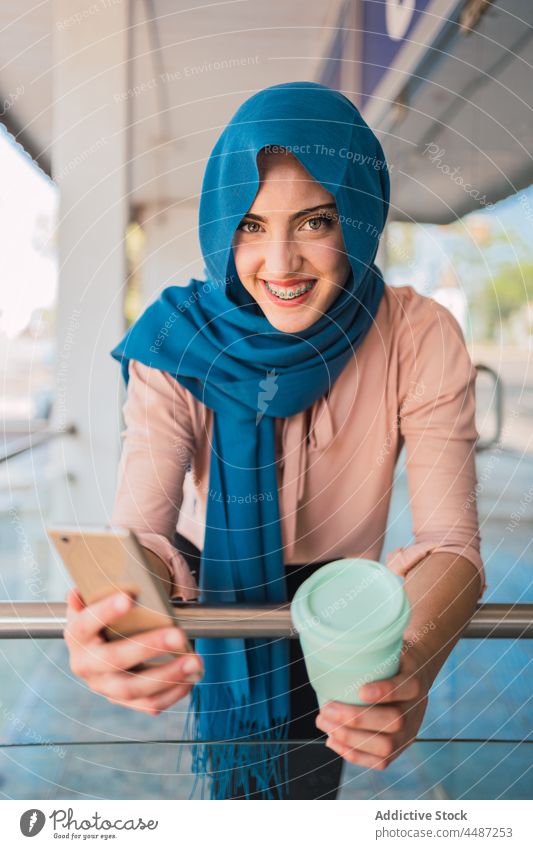 Muslimische Frau mit Kaffee zum Mitnehmen und Smartphone Imbissbude Großstadt Browsen Hijab Lächeln Mobile Telefon ethnisch arabisch muslimisch Straße online