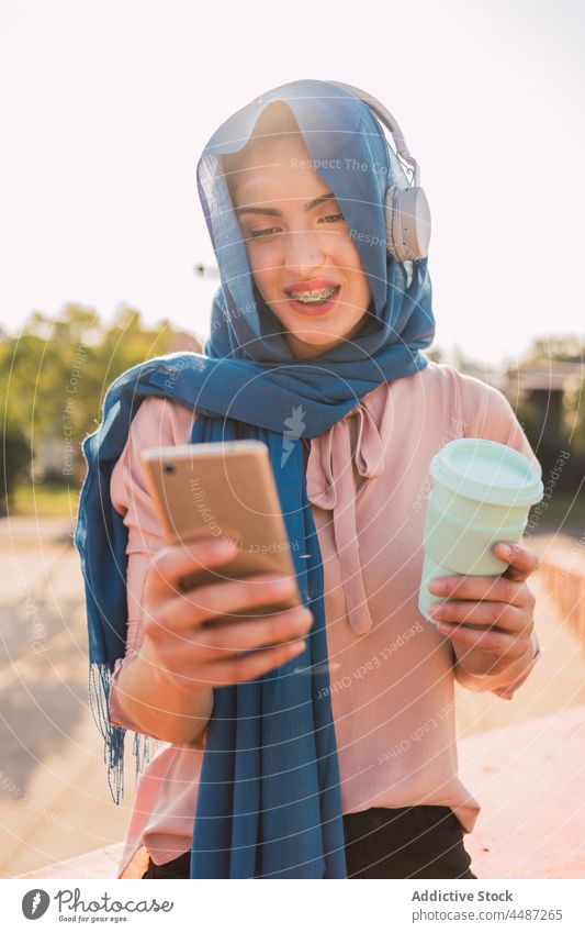 Muslimische Frau surft in der Stadt mit ihrem Smartphone im Internet zuhören Musik Kopfhörer Hijab benutzend Browsen Kopftuch Großstadt muslimisch arabisch