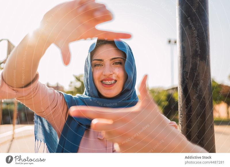 Muslimische Frau zeigt einrahmende Geste Rahmen Zeichen gestikulieren Foto Symbol Kopftuch Hijab Lächeln zeigen ethnisch arabisch muslimisch positiv froh Glück
