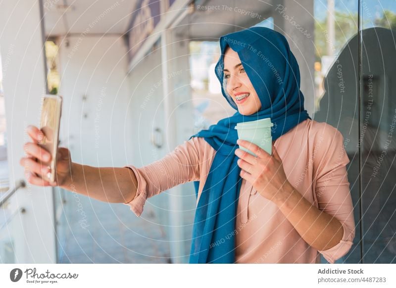 Lächelnde muslimische Frau macht Selfie in der Stadt Smartphone Hijab Imbissbude Kaffee Selbstportrait Tradition Großstadt arabisch ethnisch Straße Kopftuch