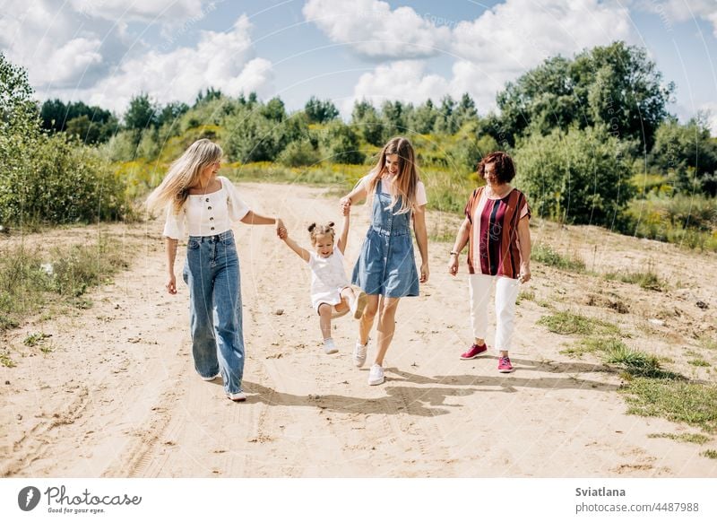 Mehrere Generationen von Frauen derselben Familie gehen auf einer unbefestigten Straße außerhalb der Stadt spazieren und genießen die gemeinsam verbrachte Zeit