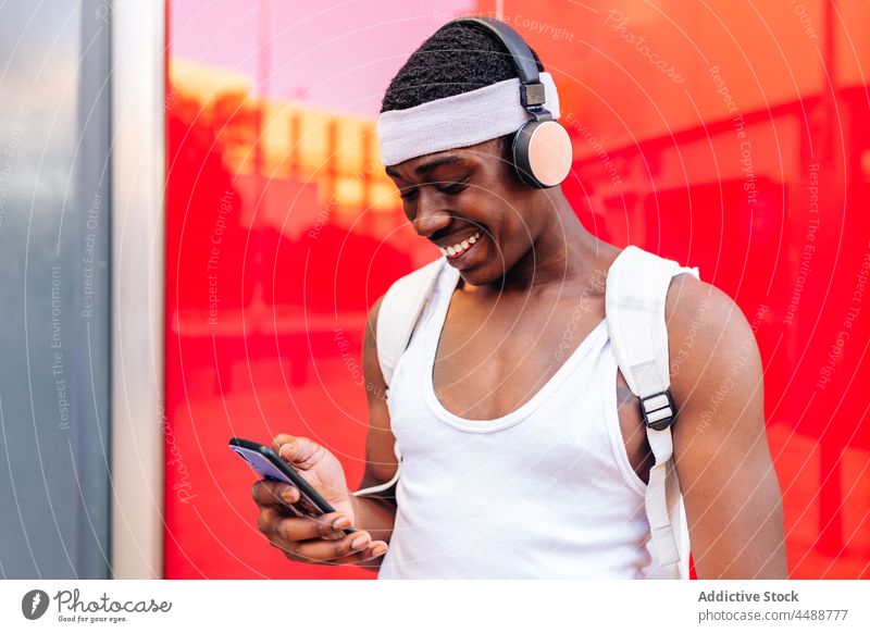Schwarzer Mann mit Kopfhörern, der auf der Straße auf seinem Smartphone surft zuhören Musik Nachricht Glück positiv froh benutzend Großstadt Inhalt Browsen