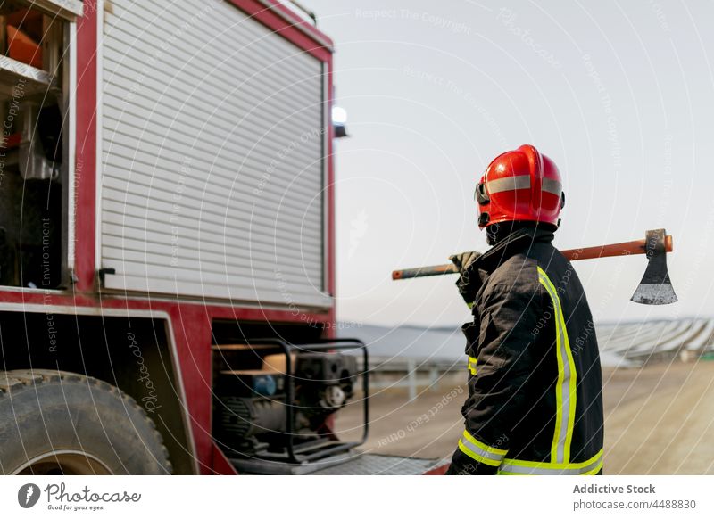 Feuerwehrmann in der Nähe des Löschfahrzeugs stehend Lastwagen Uniform Axt Gerät Job Beruf Mut Feld Landschaft Natur Schutzhelm behüten Sicherheit professionell