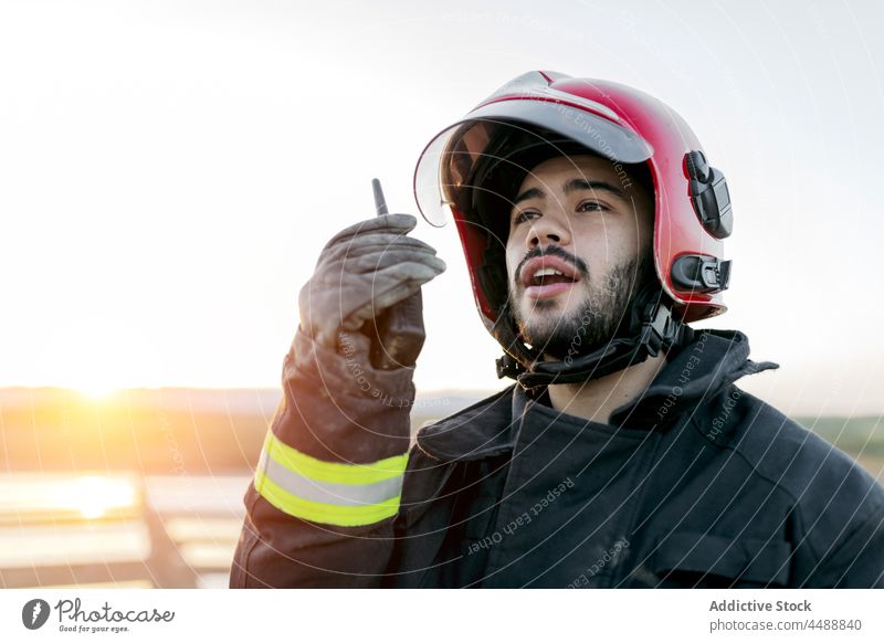 Junger Feuerwehrmann spricht in einen Sender Mann Schutzhelm sprechen Uniform Bericht Walkie-Talkie professionell Beruf Job Karriere Handschuh positiv männlich