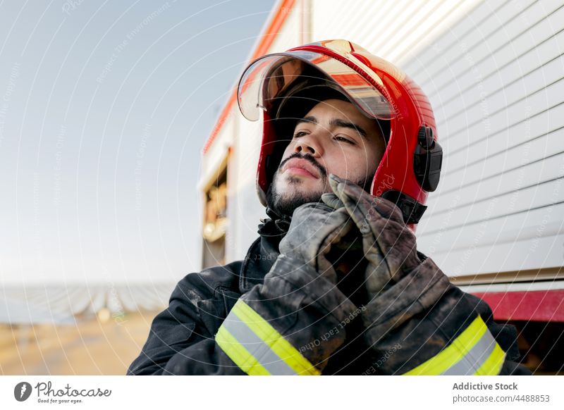 Gut aussehender Feuerwehrmann beim Einstellen des Schutzhelms Mann selbstbewusst Beruf Uniform professionell Notfall männlich behüten Lastwagen Handschuh