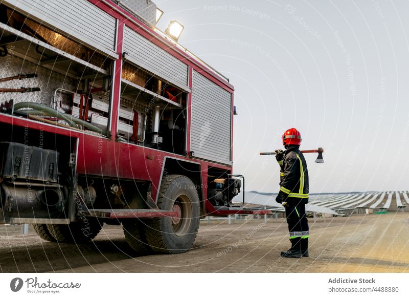 Feuerwehrmann in der Nähe des Löschfahrzeugs stehend Lastwagen Uniform Axt Gerät Job Beruf Mut Feld Landschaft Natur Schutzhelm behüten Sicherheit professionell