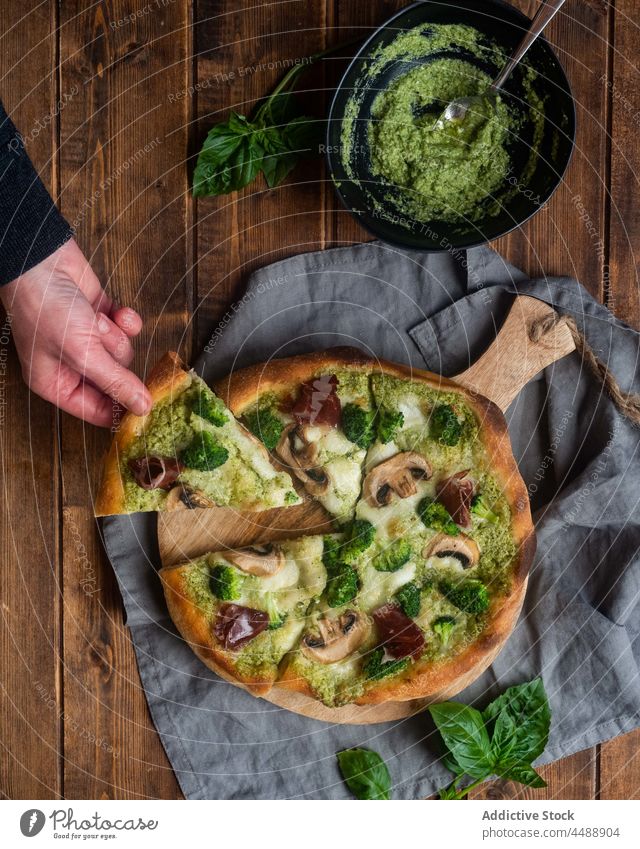 Crop Person mit einem Stück vegetarischer Pizza Vegetarier Pesto Saucen Pilz Brokkoli Scheibe Spielfigur Tisch geschmackvoll lecker Küche dienen Mahlzeit