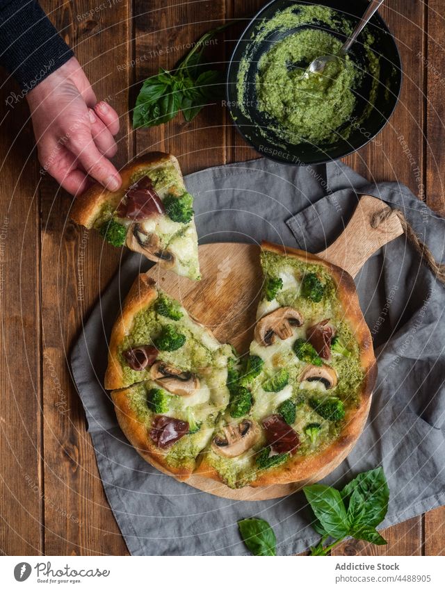 Crop Person mit einem Stück vegetarischer Pizza Vegetarier Pesto Saucen Pilz Brokkoli Scheibe Spielfigur Tisch geschmackvoll lecker Küche dienen Mahlzeit