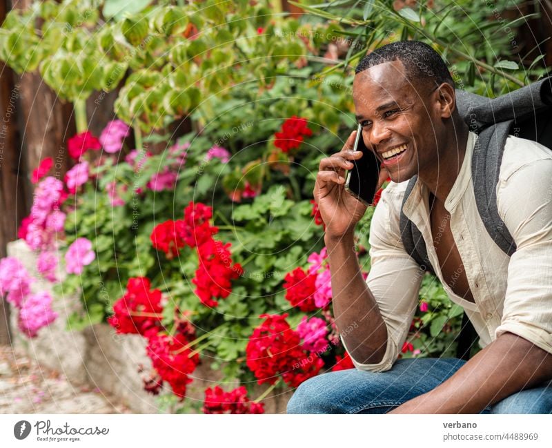 Afroschwarzer junger fitter glücklicher Mann mit Rucksack, sitzt und spricht mit einem Smartphone Telefon Technik & Technologie männlich Hintergrund Mobile