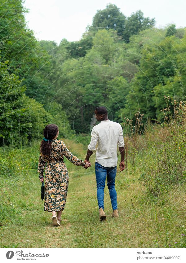 Ethnisches Paar, das sich an den Händen hält und im Herbst in einem Park spazieren geht Afro-Look Kaukasier vielfältig Liebe Familie neue Bestellung Kultur
