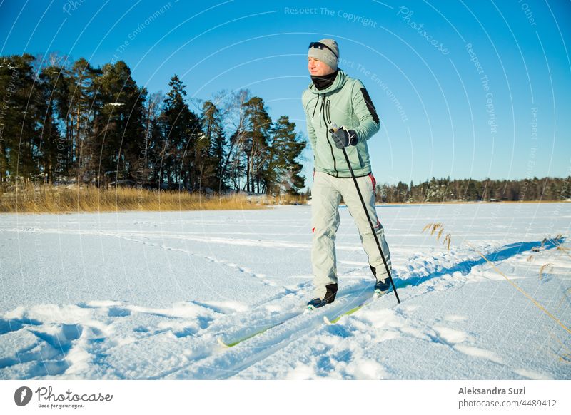 Wintersport in Finnland - Skilanglauf. Hübscher fitter Mann beim Skifahren im sonnigen Winter. Gefrorener See und Wald mit Schnee bedeckt. Aktive Menschen im Freien. Scenic friedliche finnische Landschaft.