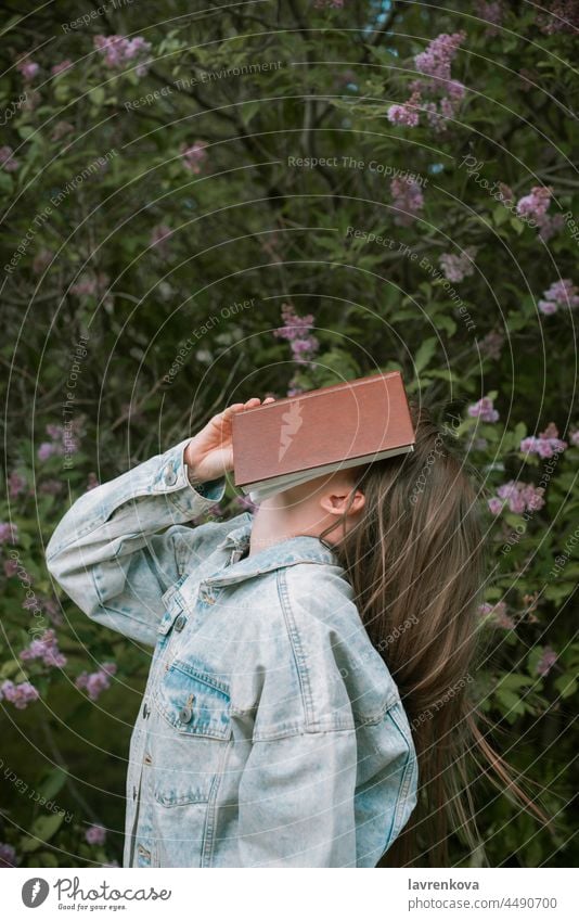 Gesichtslose Aufnahme einer Frau, die sich im Freien ein Buch vor das Gesicht hält, Lifestyle jung lesen Porträt Bildung intelligent Stehen grün Sommer Hände