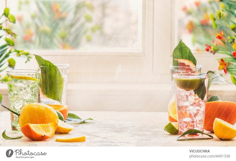 Geeiste Zitrusgetränke mit Minze, Orange und Grapefruit auf Küchentisch am Fenster mit natürlichem Licht. Hausgemachte gesunde Limonade mit Früchten im Sommer. Getränk Hintergrund mit Kopie Raum. Vorderansicht.