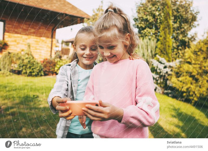 Zwei kleine Mädchen unterhalten sich vor ihrem Haus über ein Mobiltelefon mit Freunden oder Eltern über eine Videoverbindung. Selfie Kinder Smartphone Adoption