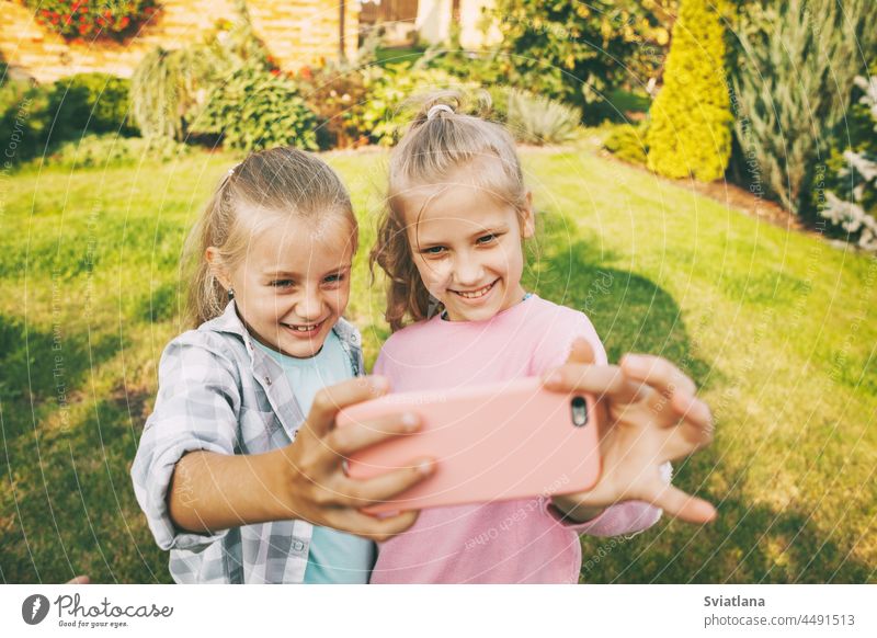 Zwei glückliche Mädchen im Teenageralter lachen und machen ein Selfie mit einem Handy im Freien. Kinder Smartphone Adoption Menschen Bildung Schule Freizeit