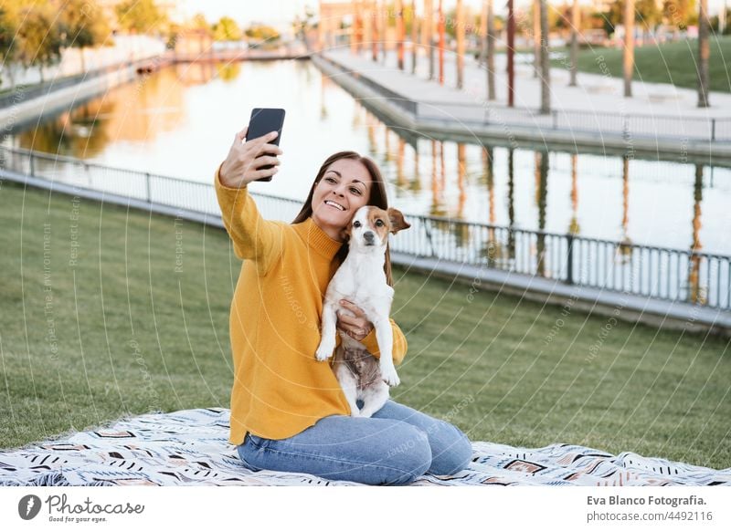 Frau hat Spaß mit Jack-Russell-Hund im Park, sitzt auf einer Decke während der Herbstsaison. Frau fotografiert mit Handy. Haustiere und Liebe Konzept